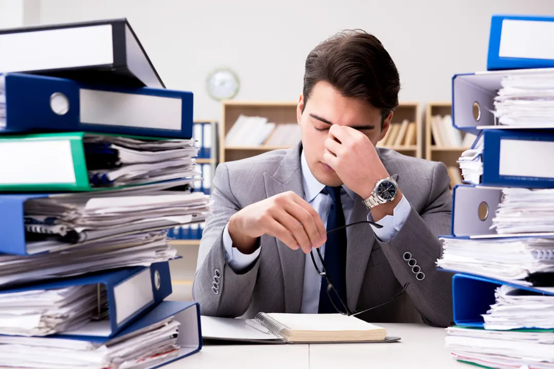 Stressed worker sits amid stacks of binders