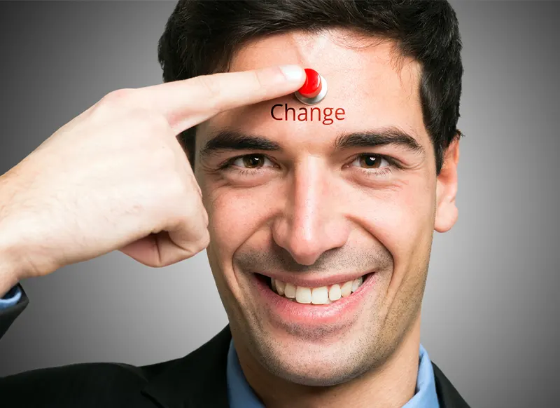 A smiling man with brown eyes and 5 o'clock shadow presses a bright red button on his forehead labeled 