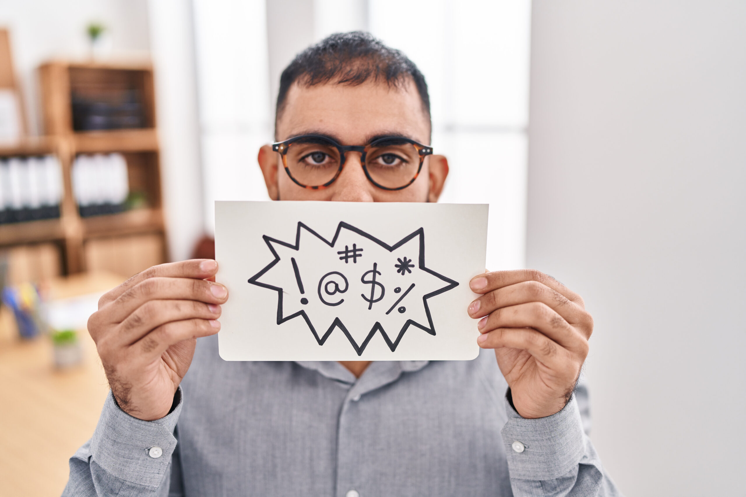 man holds card with signs indicating foul language