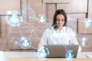 A young female businesswoman in a white collared shirt looks down at a laptop while communicating and connecting with people virtually all over the world