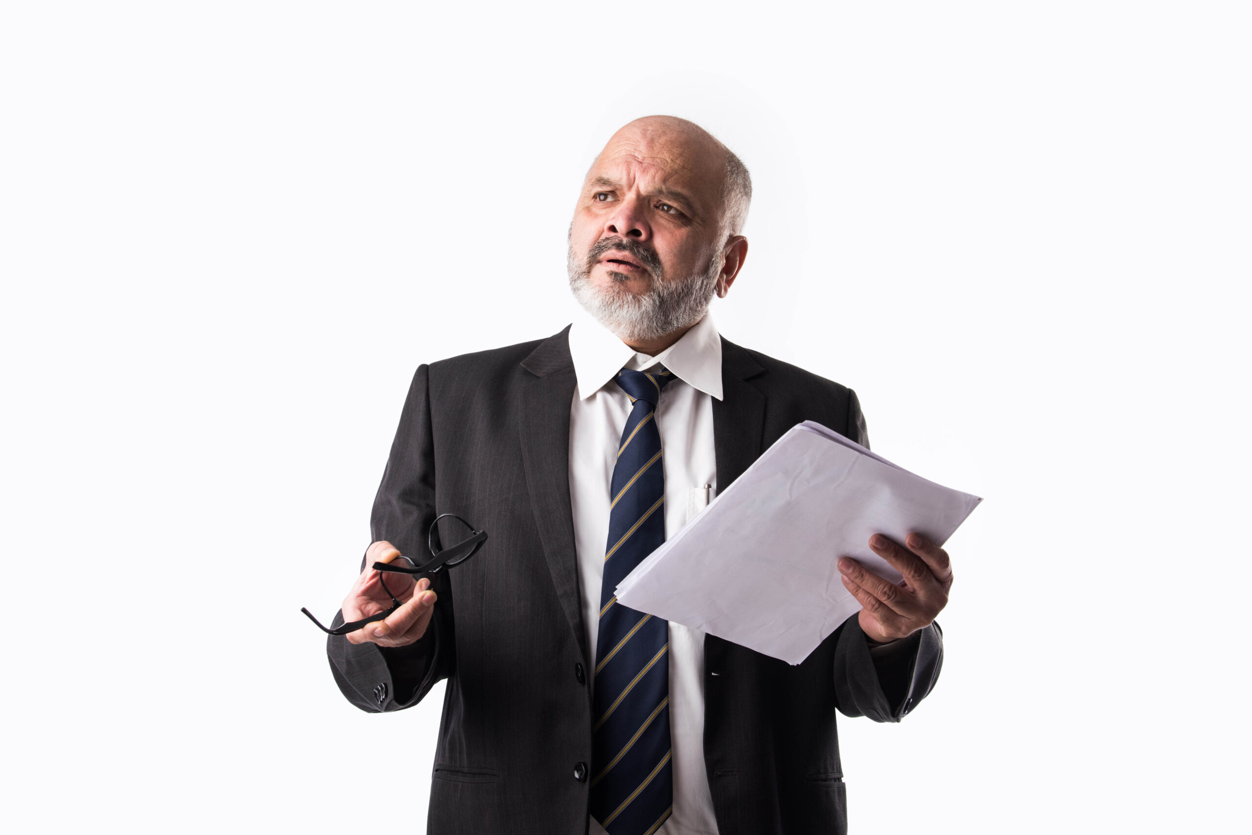 A businessman in a suit and tie holds his glasses and a stack of papers while thinking about what to do and say next