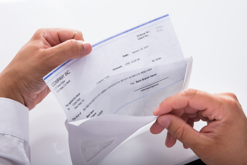 A man in a white dress shirt opens an envelope with his pay check