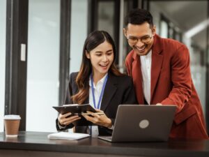 A smiling woman and a man with glasses look at something on a laptop screen