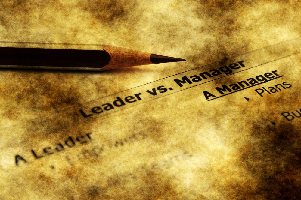 A pencil lays above text that reads "Leader versus Manager"