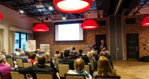 A man in a business suit speaks into a microphone in front of a group of seated people