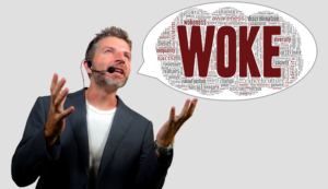 A senior executive in a suit without a tie holds up his hands and says "Woke"