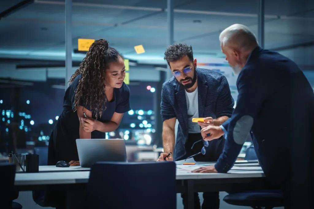 Three entrepreneurs, one woman and two men, stand around a table talking about their strategic go-to-market plan.