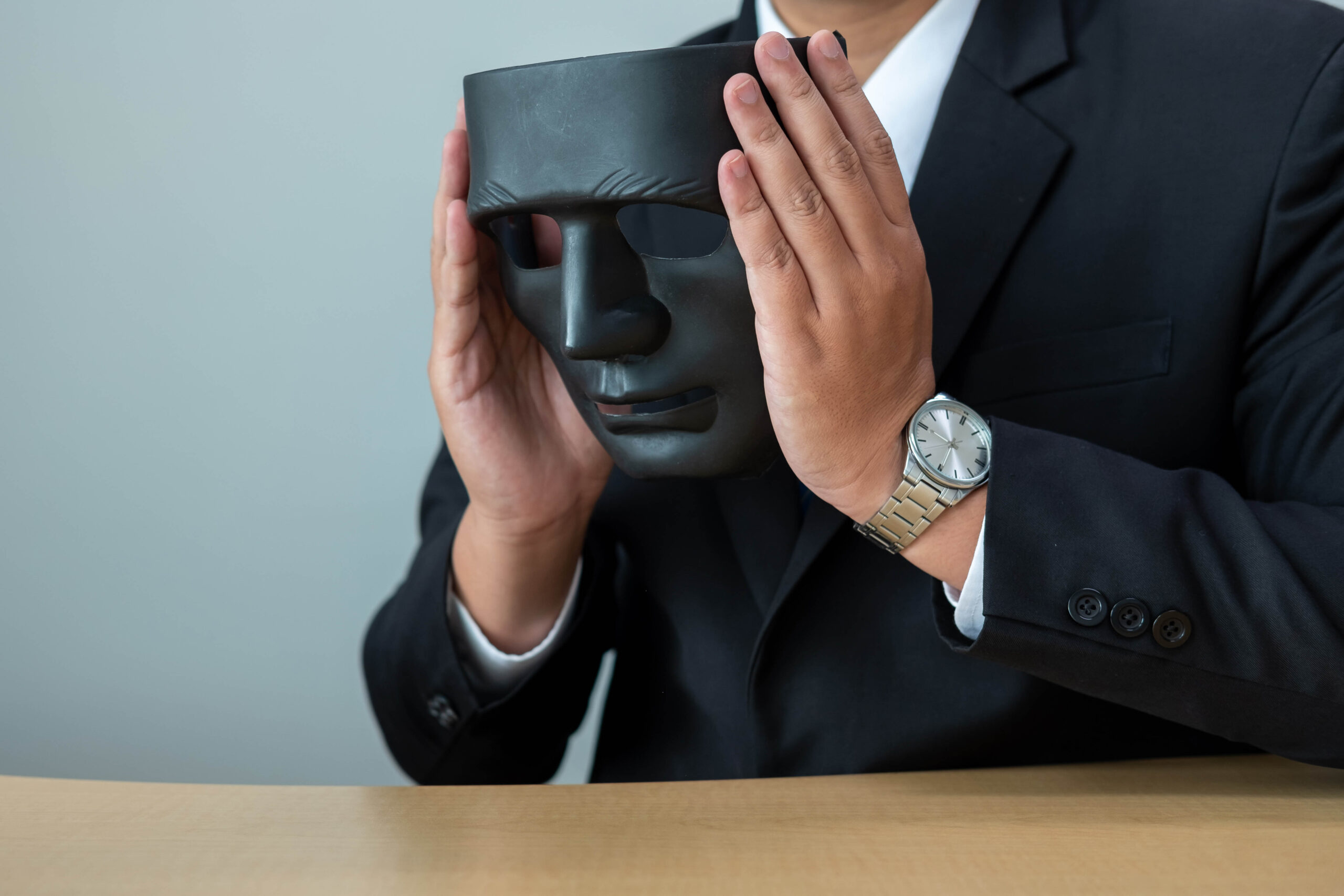 A businessman in a suit and tie who had made a DEI commitment but reneged on it holds a black mask