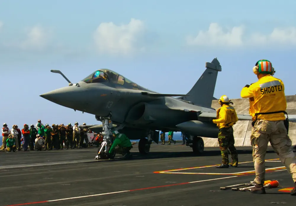 An air-traffic controller dressed in yellow signals to a fighter jet about to take off from an aircraft carrier.