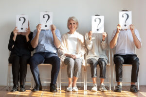 A female candidate waits to be called in for a job interview while candidates holding a question mark in front of their faces sit next to her.