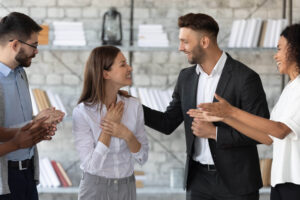 A young female entrepreneur smiles while being congratulated and supported by a group of young male and female businesspeople.