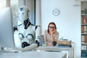 A woman in glasses with a frustrated or annoyed facial expression sits at her desk behind an AI robot working at a nearby desk.