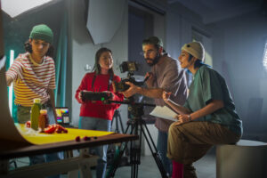 Diverse Young Filmmakers Collaborate On A Vibrant Set, Focusing On A Camera Setup While Discussing Scene Details, Reflecting Creativity And Teamwork In Modern Videography And Advertising Production.