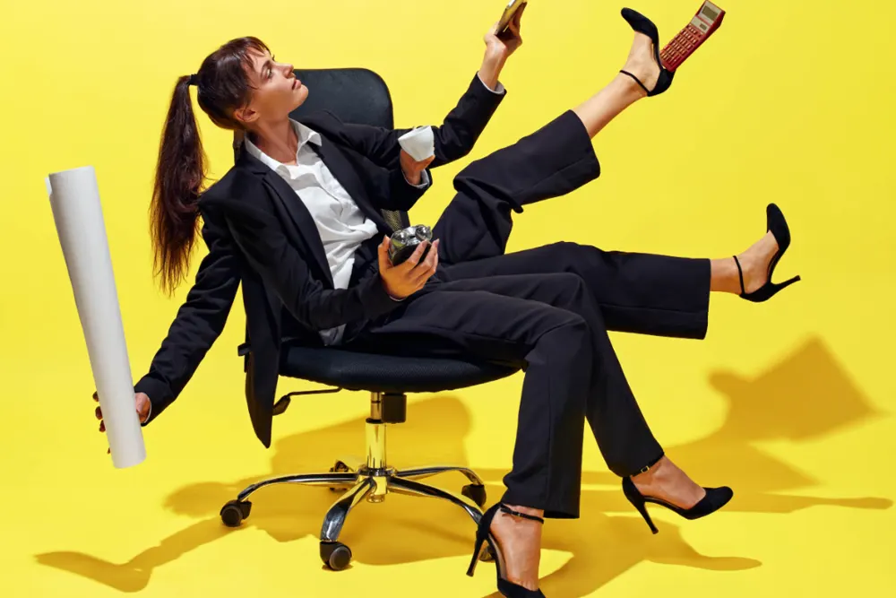 A woman in a business suit with seemingly four arms and four legs frantically multitasks with several devices.