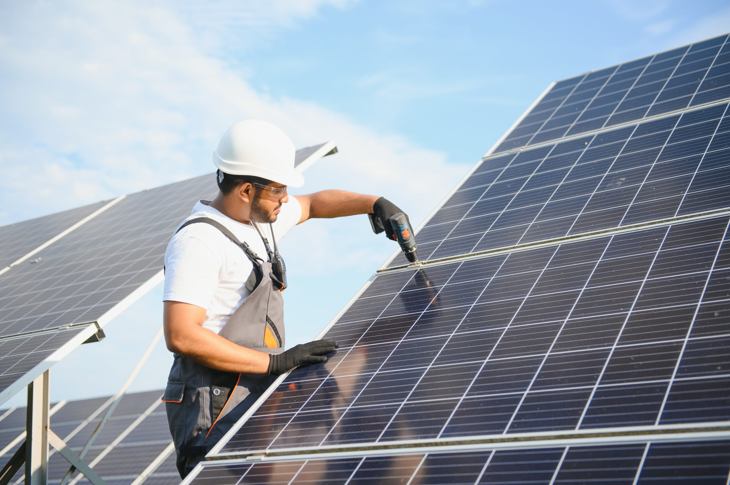 An Indian worker in uniform and with tools works on a solar panel farm.