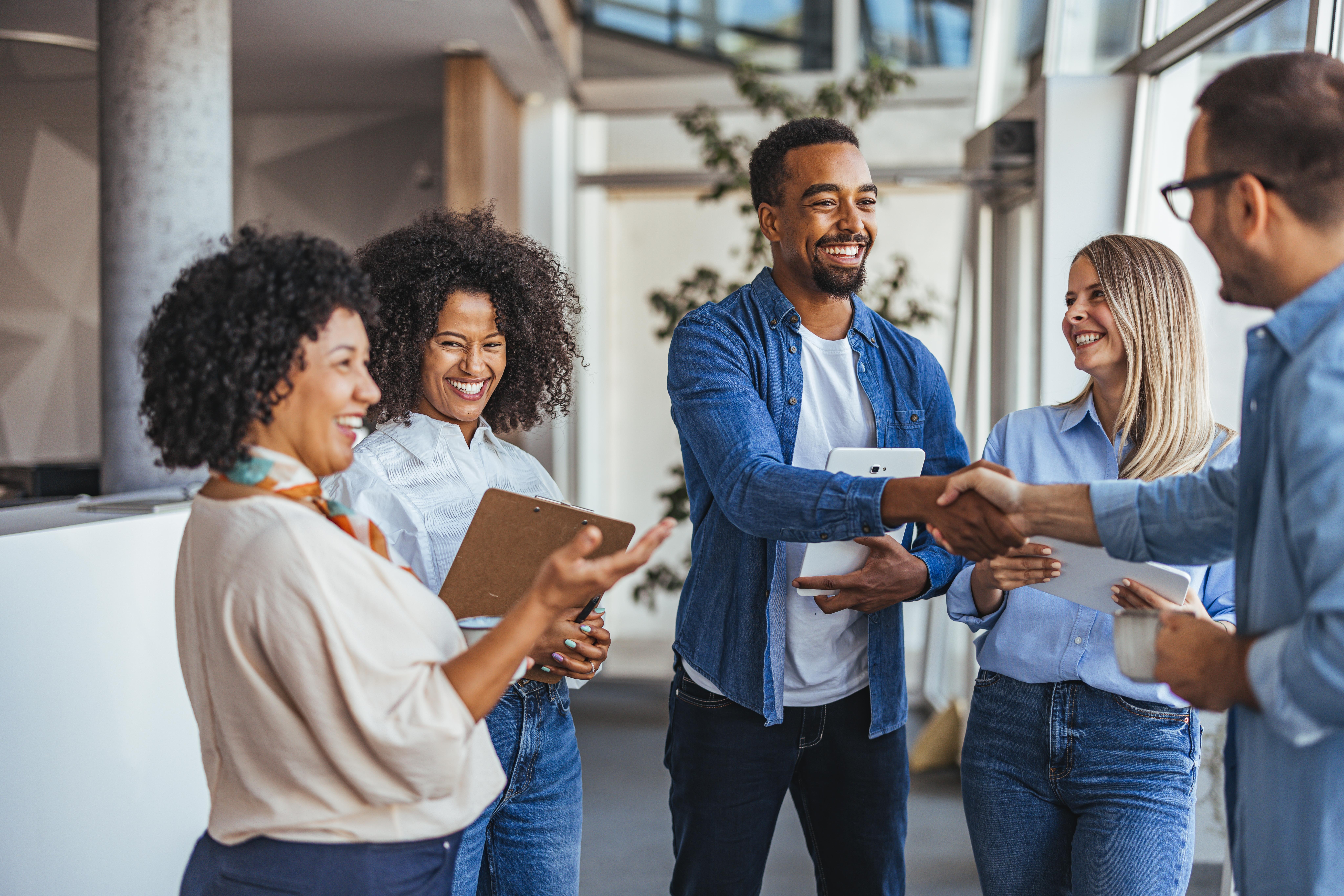 Diverse group of professionals smiling and shaking hands modern office environment teamwork collaboration positive business relationships