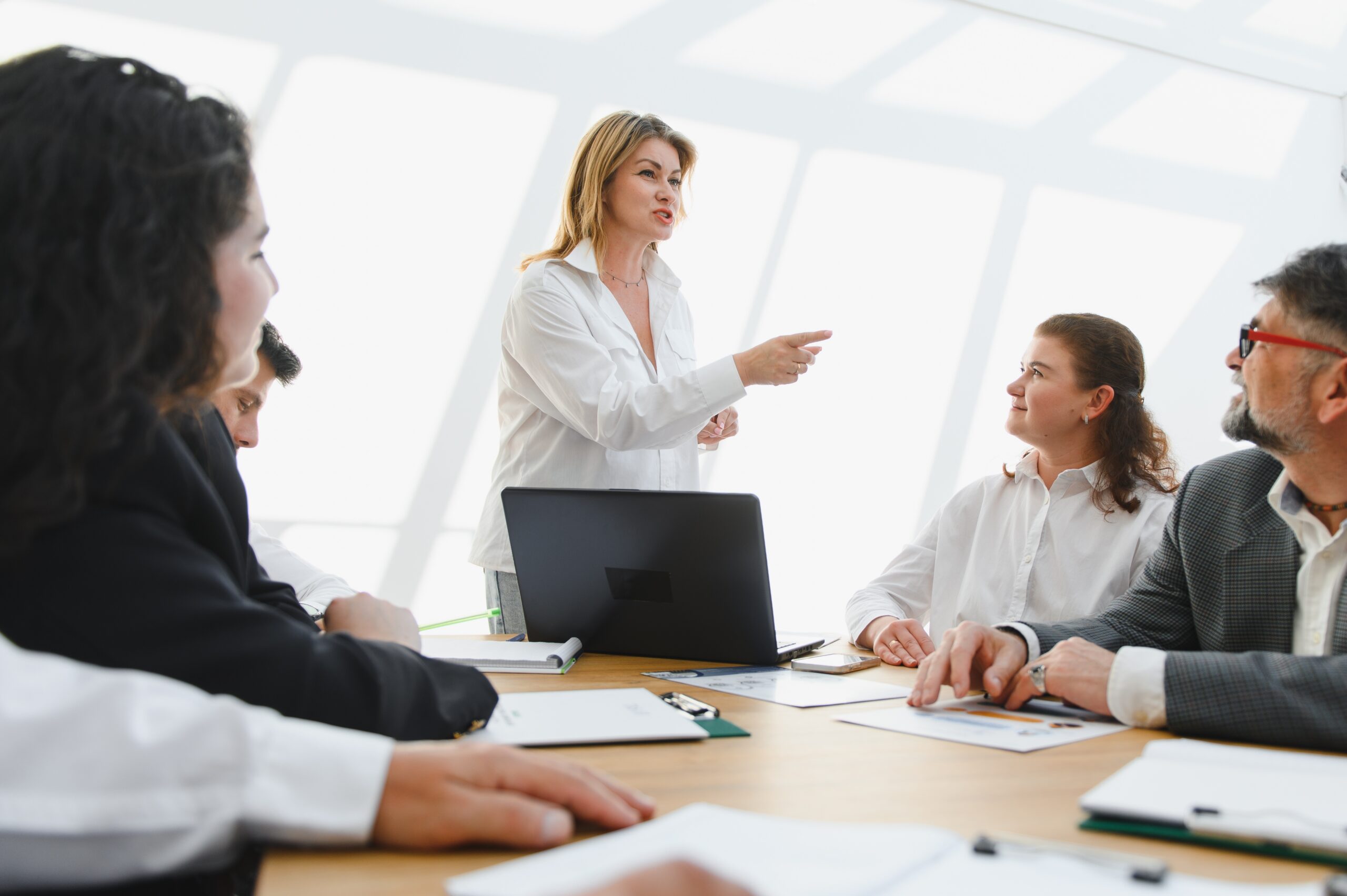 Female executive leading a business meeting, addressing colleagues and pointing towards future goals, fostering collaboration and strategic decision making in contemporary workspace