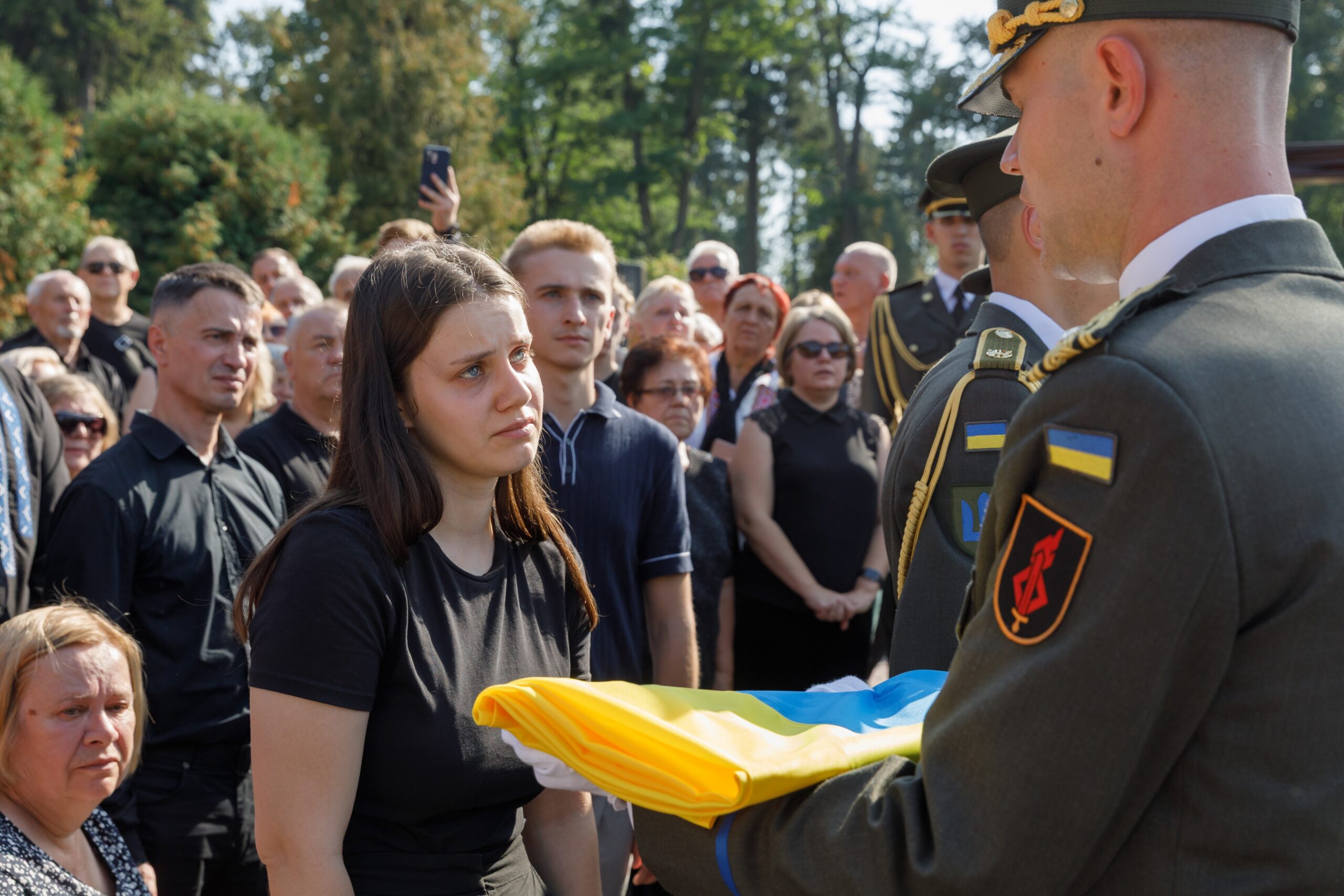 Lviv, Ukraine - Sep. 02, 2025: Mourners express their sorrow as a soldier presents a Ukrainian flag during the funeral ceremony for Andriy Parubiy at Lychakiv Cemetery in Lviv.