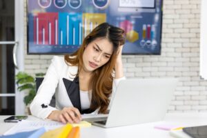 Serious businesswoman working on her computer at her desk inside modern office. Unhappy Asian woman with busy and trouble in her work.