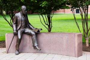 WORCESTER, MA, USA - July 07, 2009: Bronze statue depicting Sigmund Freud sits on a granite bench in a vibrant urban park. The sculpture features Freud holding a cane, with an open book beside him and lush greenery all around.