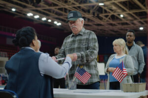 Elderly man talks with polling officer and takes vote bulletin. Multi cultural American citizens come to vote in polling station. Political races of US presidential candidates. National Election Day