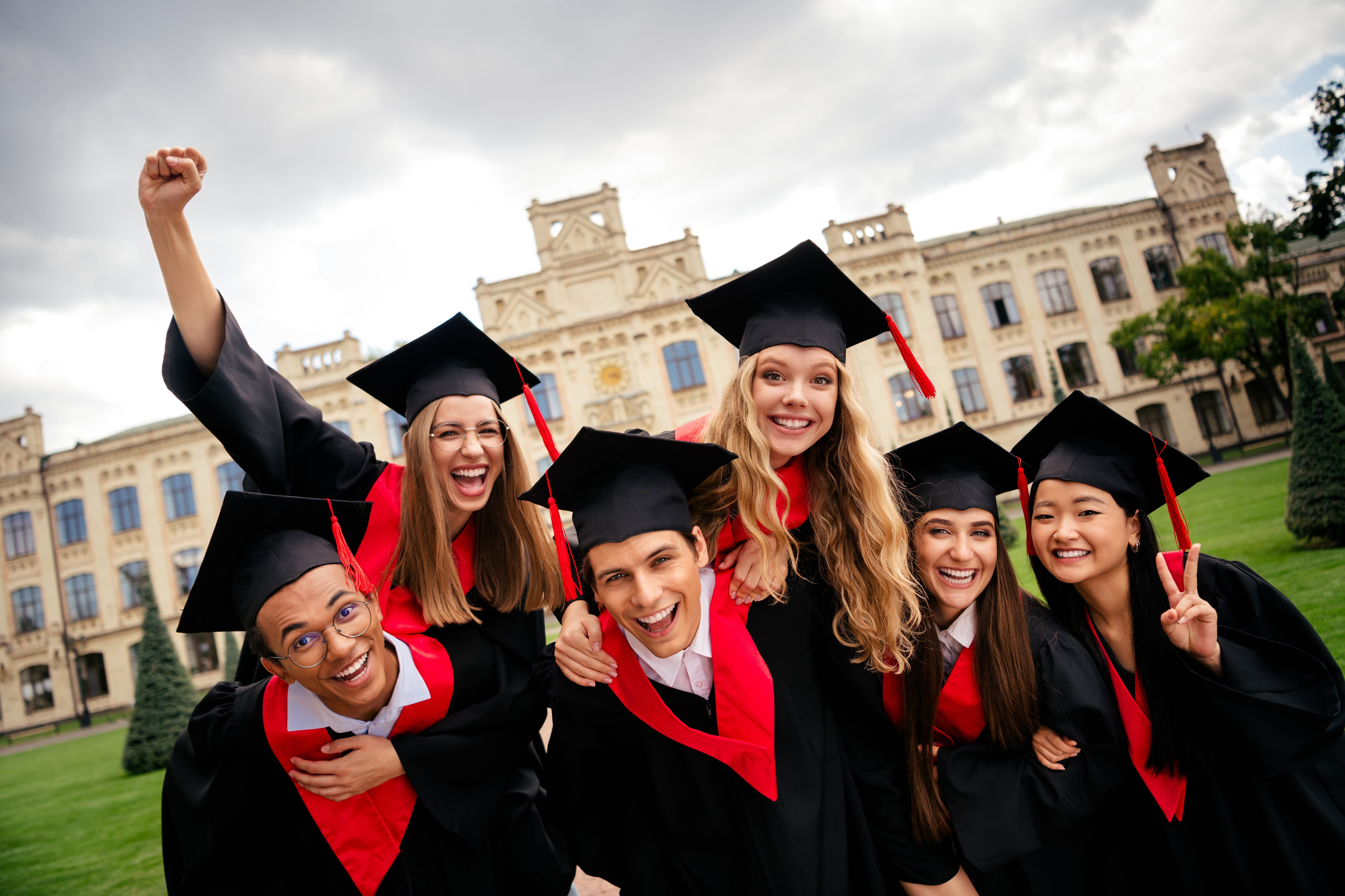 Joyful group of young graduates celebrating outside historic university building on a sunny summer day